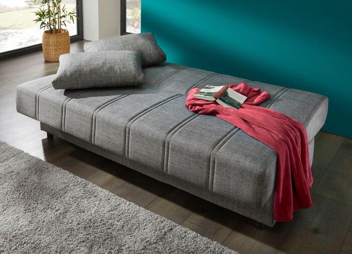 Frei im Raum aufstellbares Schlafsofa mit Dekokissen und Bettkasten 